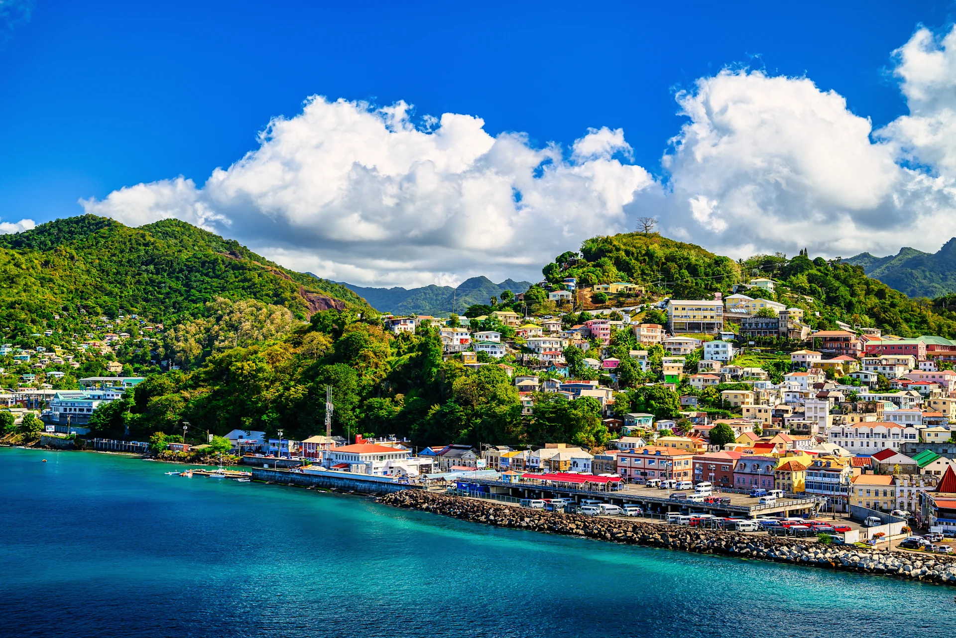 The capital of Grenada set amongst green mountains seen from across vibrant blue water.