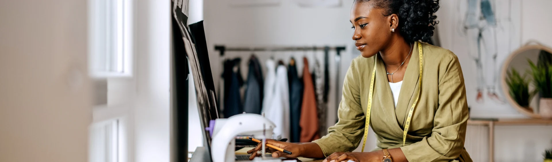 Young female presenting person sits at a desk with a sewing machine, operating a small business.