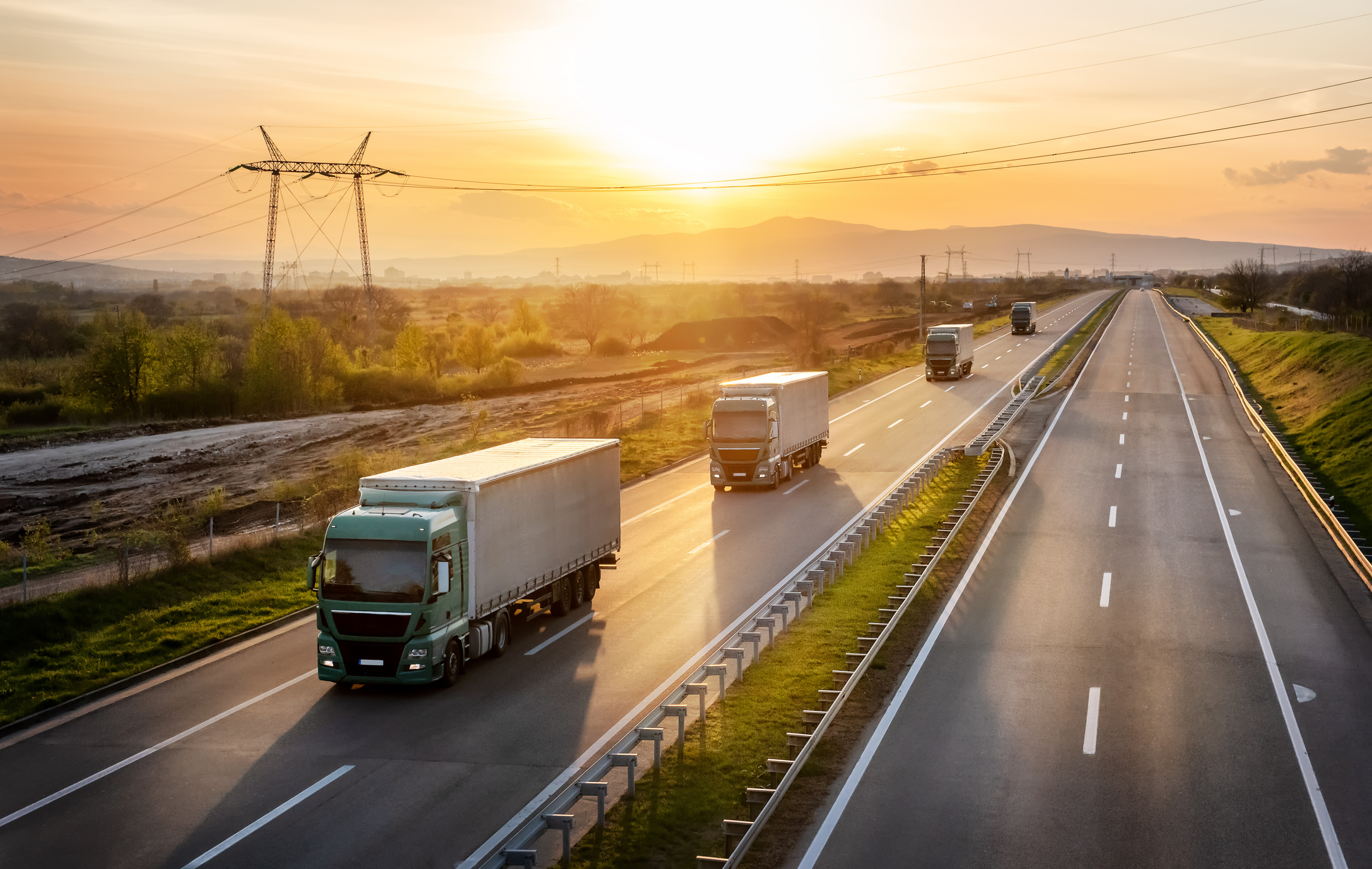 Lorries driving down an open road during sunrise.