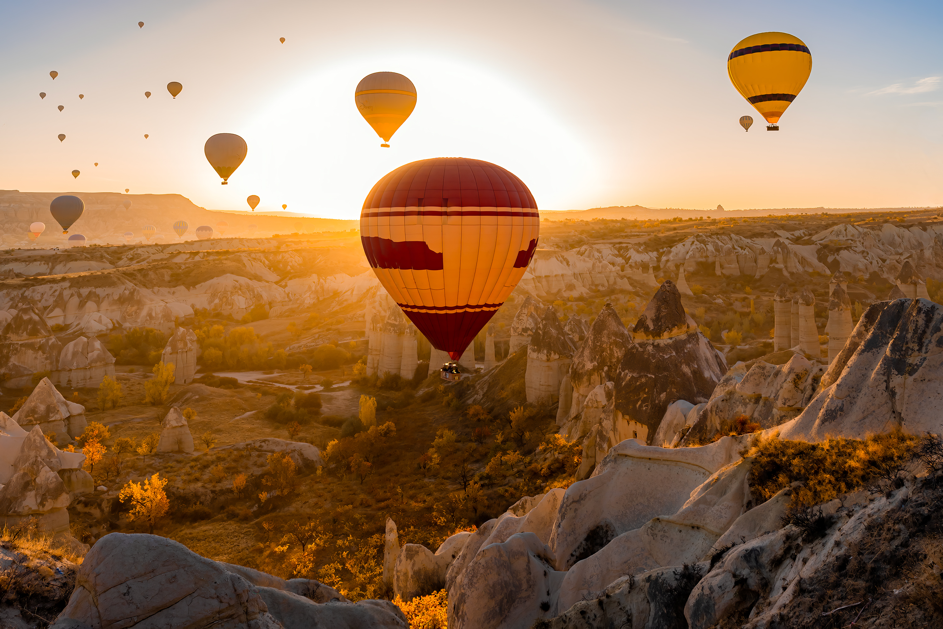 Close up of a red and yellow hot air balloon at sunset, floating over a hilly desert landscape in Turkey.