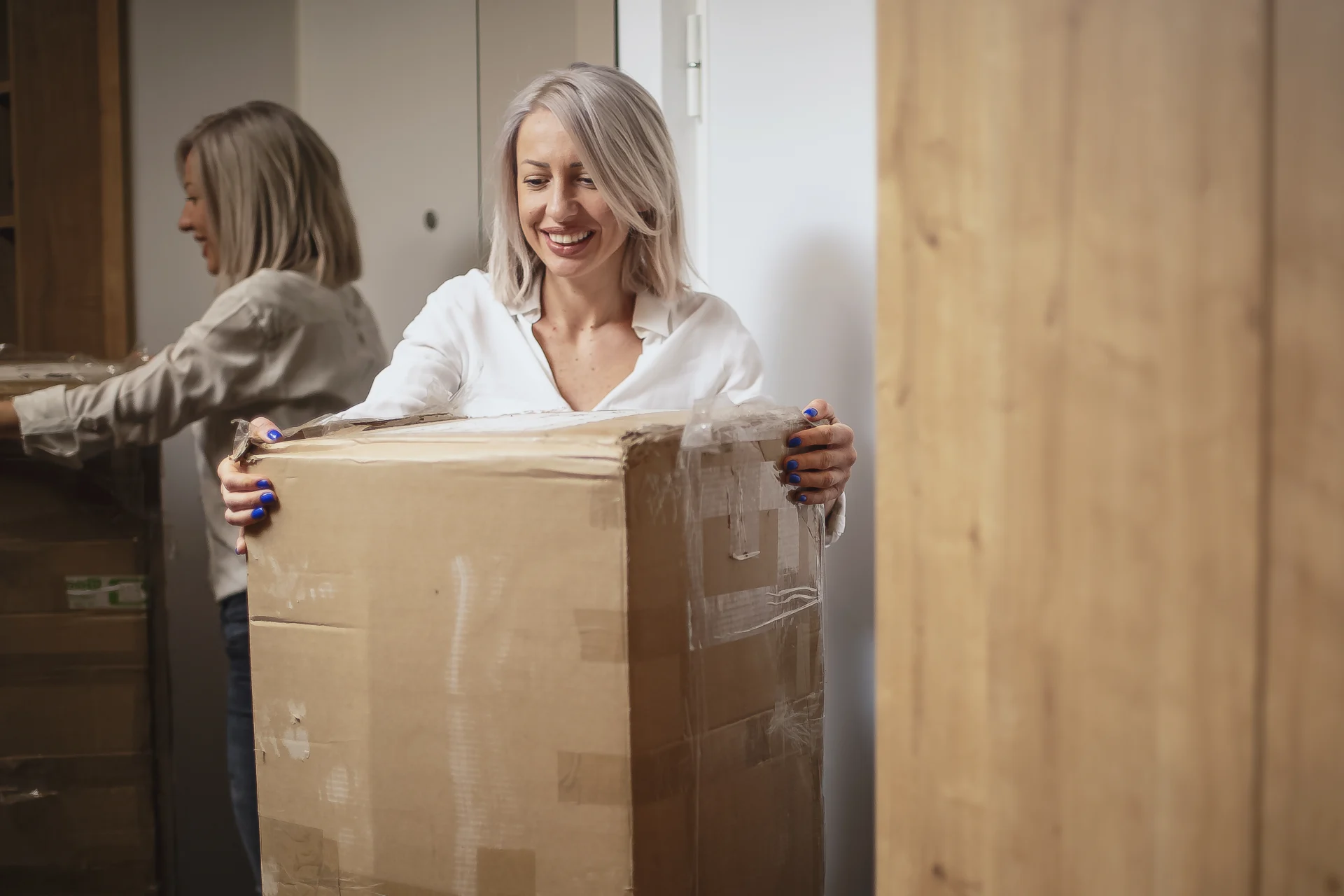 Woman with a smile and blue nail varnish moving a large boxed package