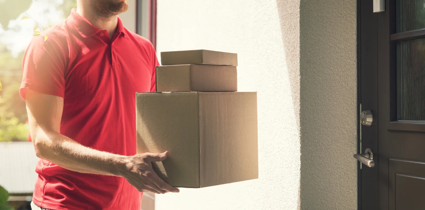 Man in red polo shirt holding a stack of 3 boxes in a doorway