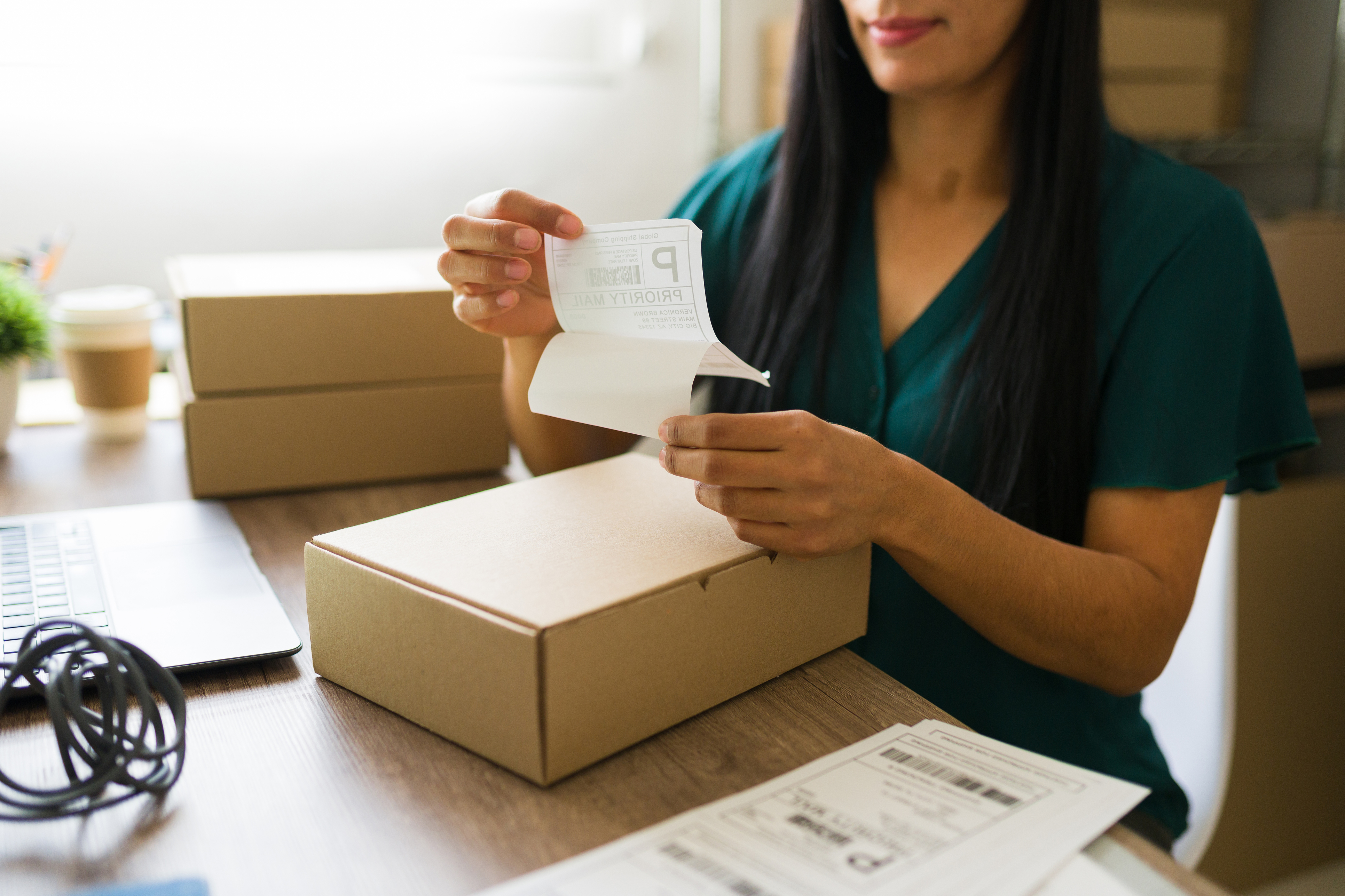 Woman in a teal dress pealing a shipping label to attach to a box