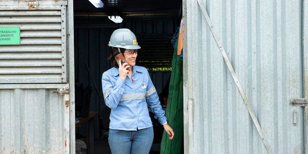 A woman in a hard hat and safety glasses talks on a mobile phone.