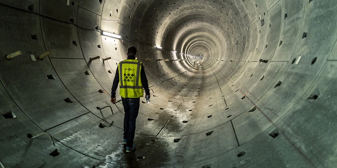 A man in a construction vest walks in an underground tunnel.