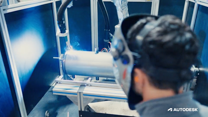 Person with welding mask looking at a welding machine working on a metal part.