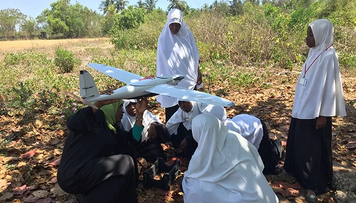 Women in Tanzania stand around a drone outside.