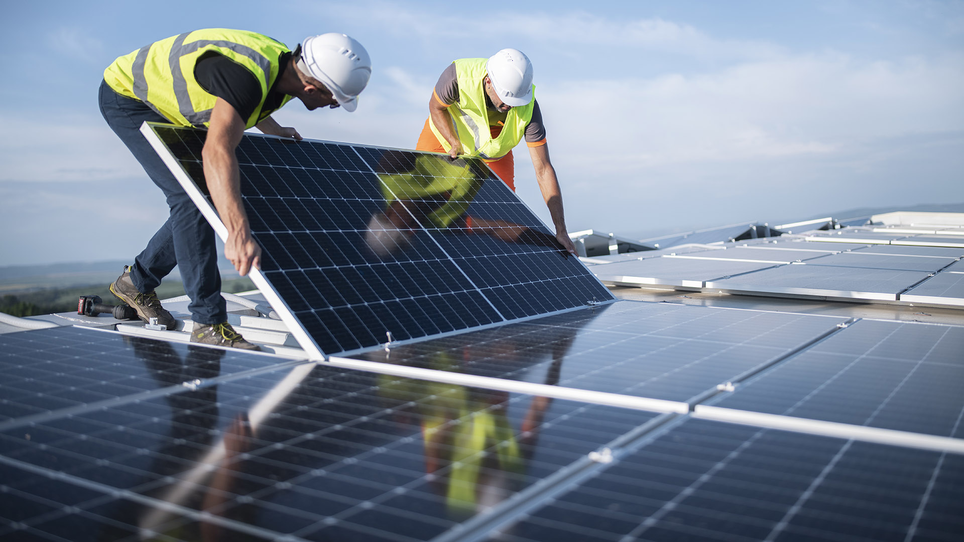 Two engineers install solar panels on roof.