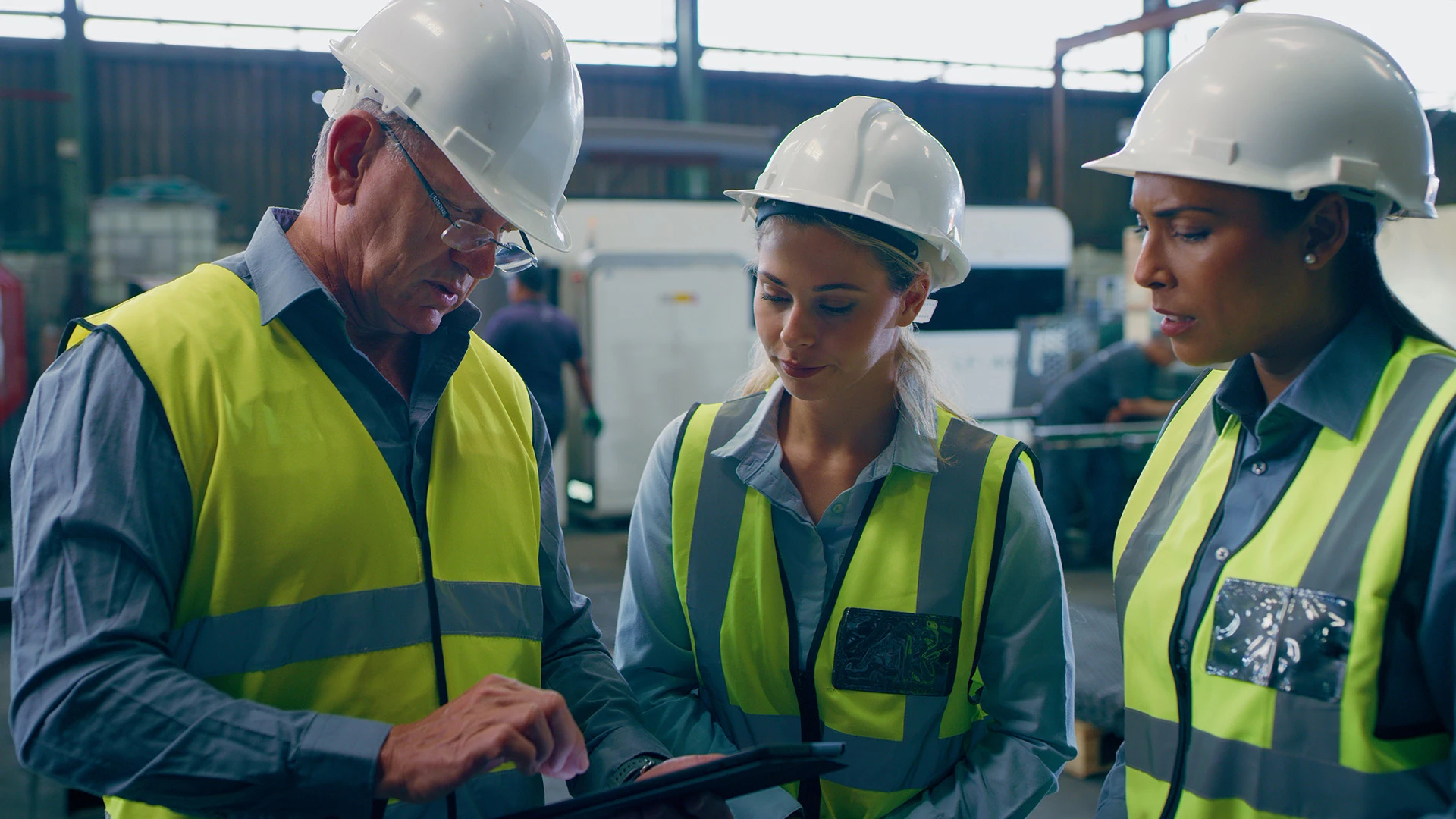 Auf einer Baustelle blicken drei Mitglieder eines Ingenieursteams, die Bauhelme tragen, auf ein Tablet.