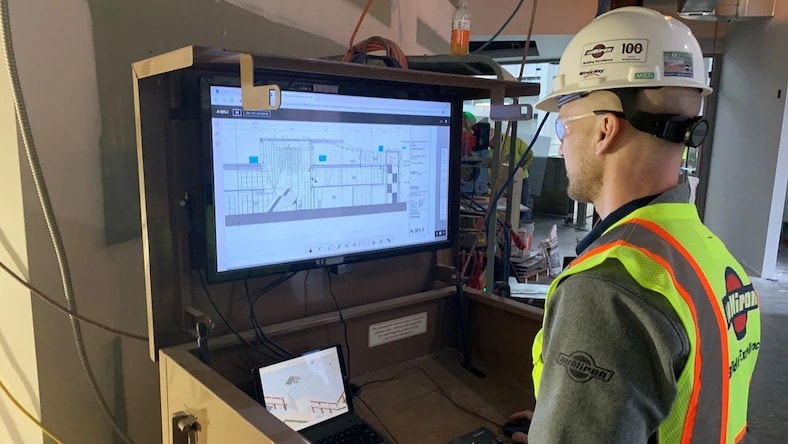 Construction work views building plans on an on-site computer monitor