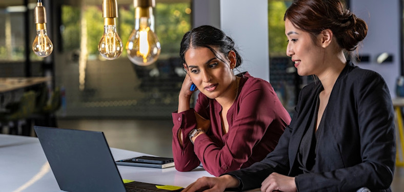 Two women discuss what they see on a laptop screen.