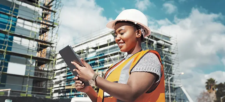 A female construction worker smiles at a tablet on a jobsite.