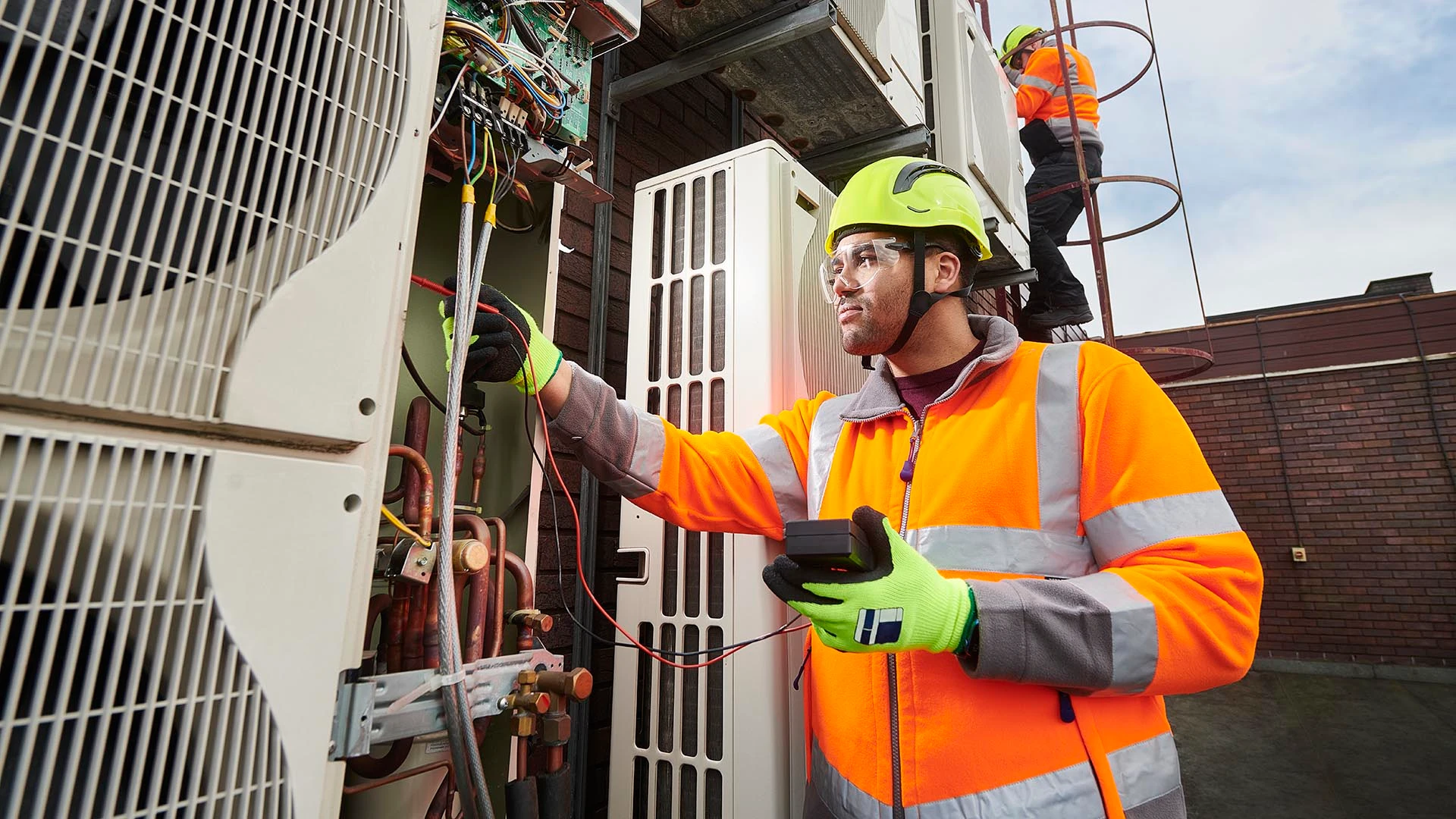 Un technicien CVC, équipé de son matériel de sécurité, inspecte et répare des unités de climatisation externes.