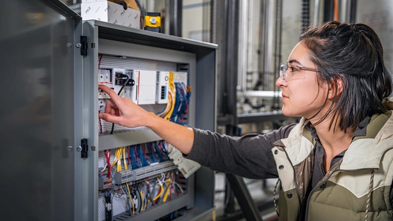 A woman adjusts an electrical panel in a power substation.