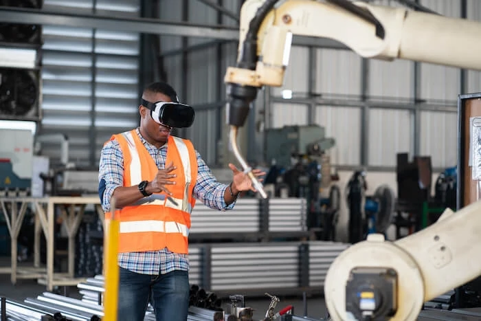 A man in VR goggles stands in front of an industrial robot.