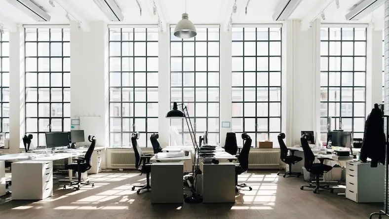 A modern office space is flooded with light from floor-to-ceiling windows.