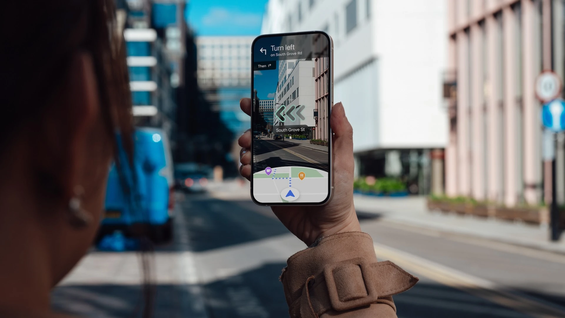 Over-the-shoulder view of a young woman holding a smartphone showing a GPS app with augmented reality technology.