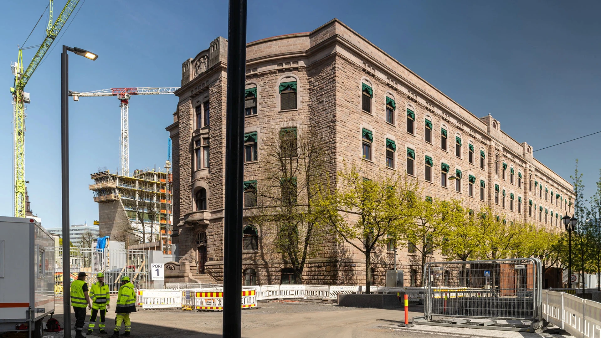 Ein historisches Steingebäude wird restauriert – in der Nähe verrichten Arbeitskräfte in Warnkleidung ihre Tätigkeiten und Baukräne werden eingesetzt.