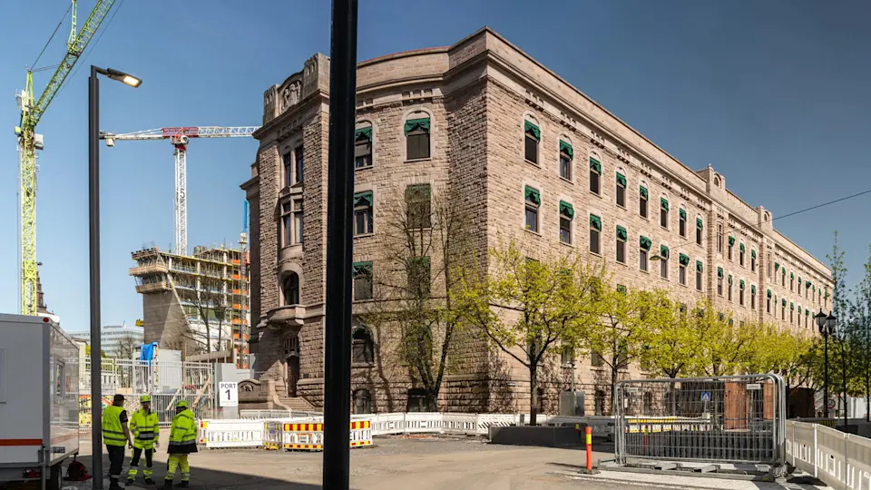 Uno storico edificio in pietra si trova in fase di restauro mentre le gru da costruzione e i lavoratori in abbigliamento ad alta visibilità lavorano attivamente nelle vicinanze.