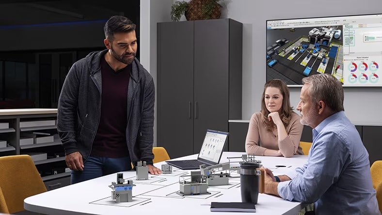 Three people around an office table displaying factory layout components.