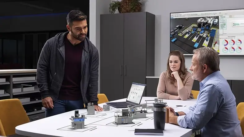Three people around an office table displaying factory layout components.