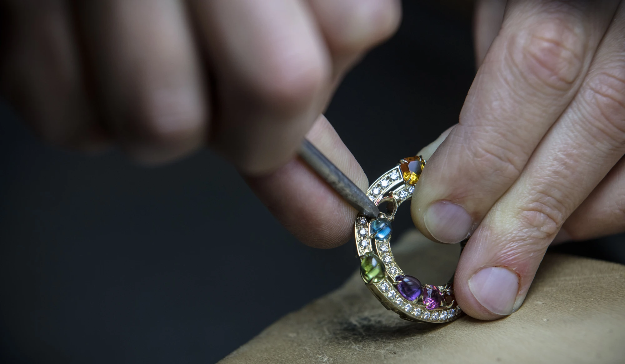 A Bulgari artist works on ring with multicolored gemstones.