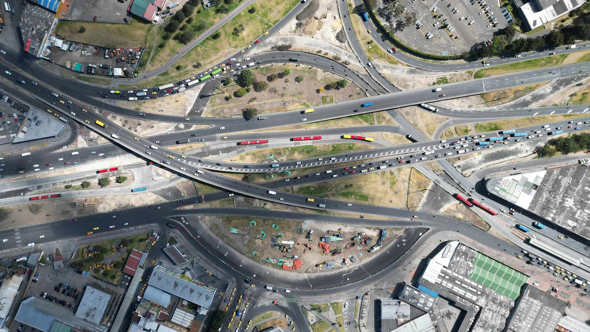 Eine Luftaufnahme eines im Bau befindlichen Autobahnkreuzes zeigt Verkehr sowie mehrere Überführungen und Schleifenrampen.