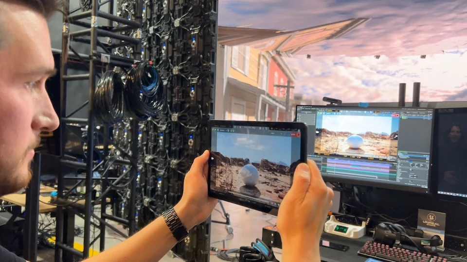 A man holds a tablet showing the camera-corrected view of the distorted virtual production setup beyond.