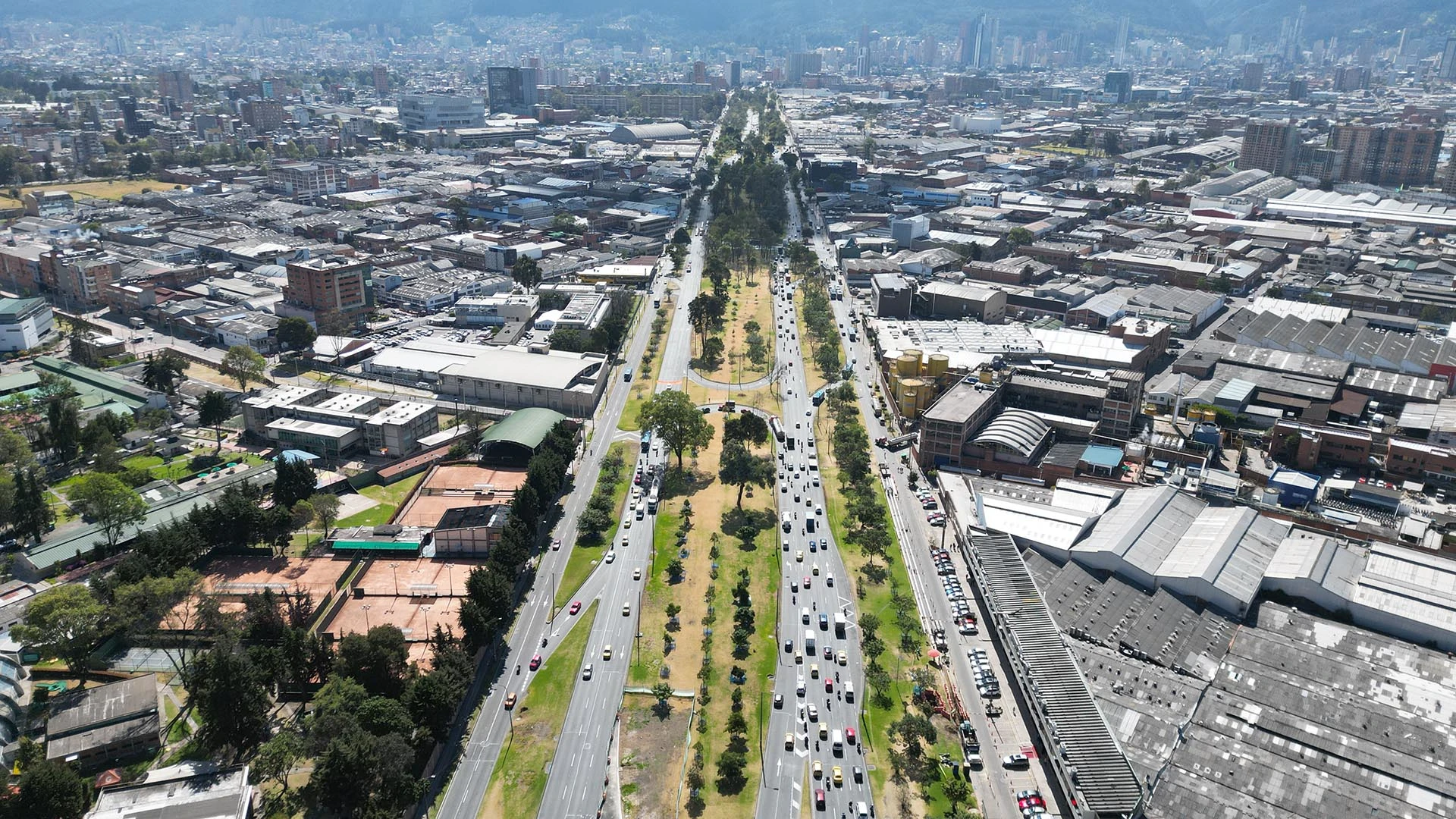 Eine Luftaufnahme zeigt einen breiten Boulevard mit Verkehr, einen von Bäumen bestandenen Mittelstreifen und umliegenden städtischen Gebäuden.