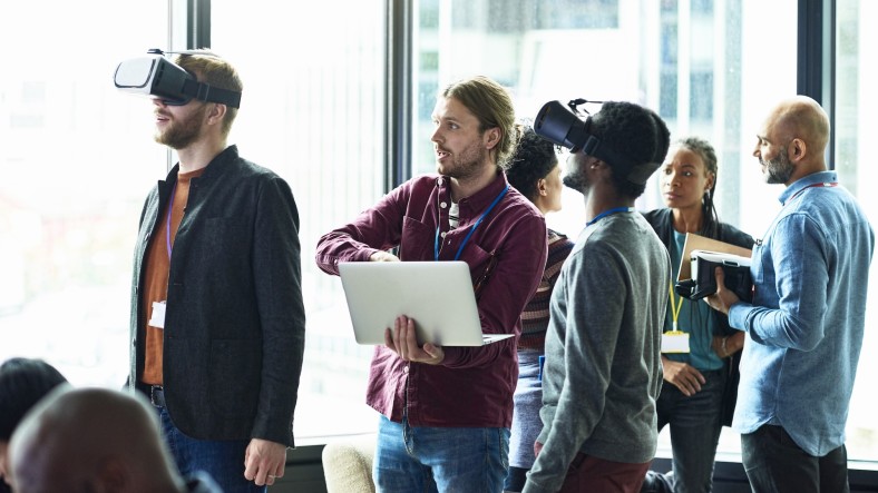 A diverse group of individual in an office setting, with two men in VR goggles