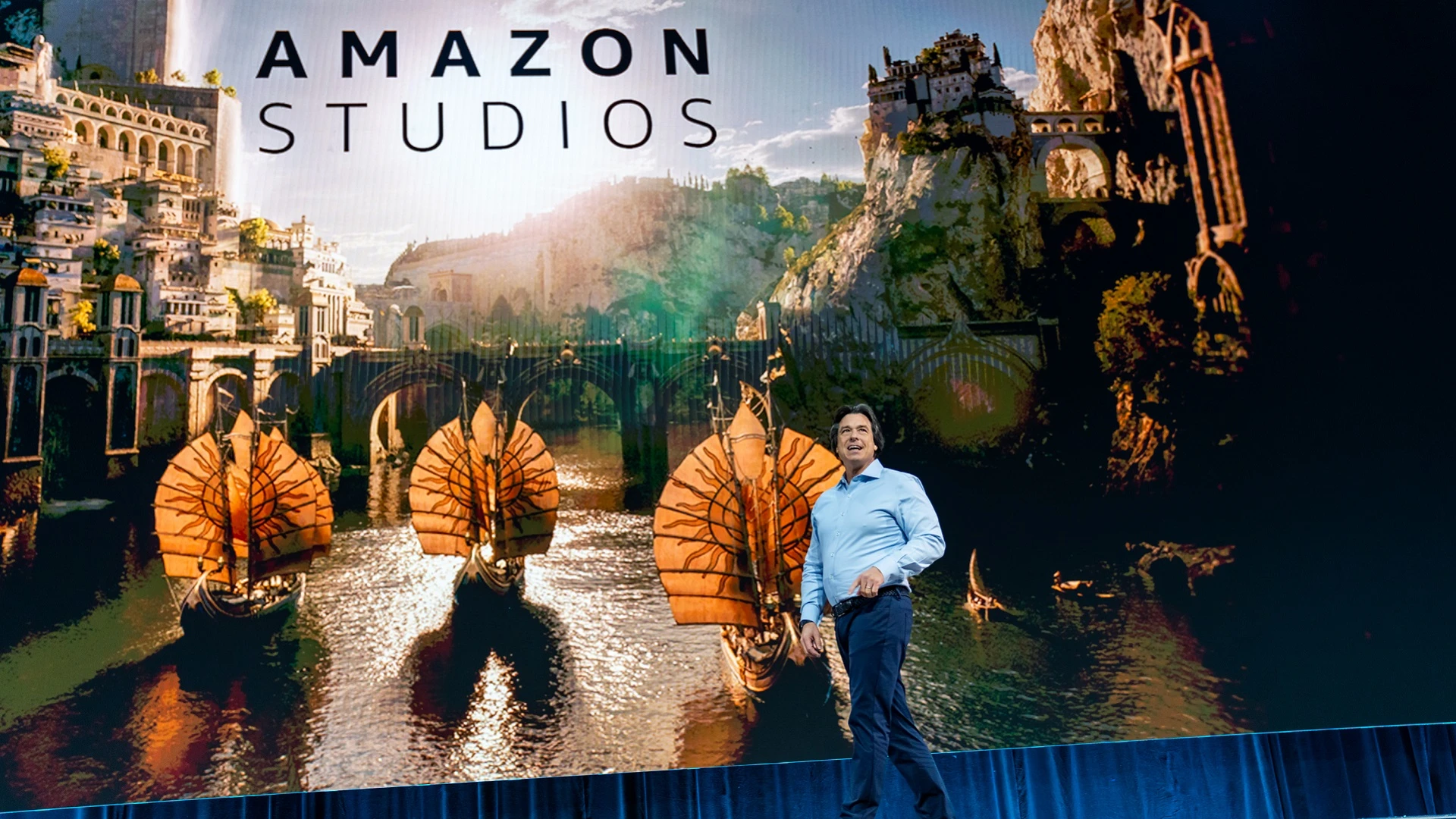 Eric Iverson of Amazon Studios in front of a scenic image from The Lord of the Rings: Rings of Power