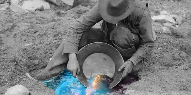 Black and white photo of a prospector panning for gold with blue digital overlay