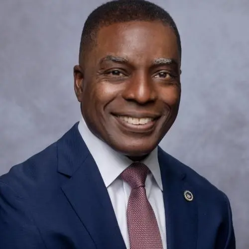 Auf diesem akademischen Studio-Porträt lächelt ein afroamerikanischer Mann in einem Anzug.