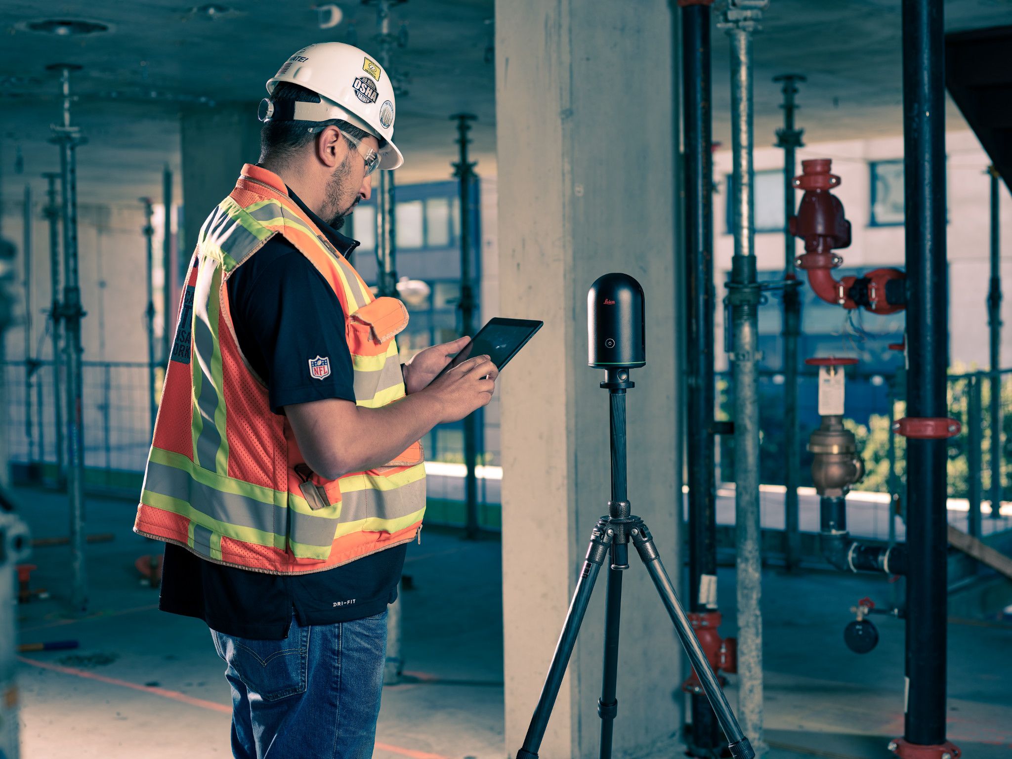A construction worker uses a tablet next to a laser-scanning device.
