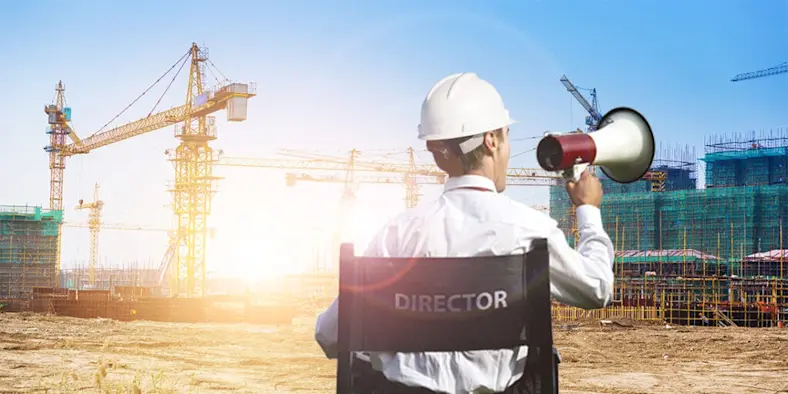 Person sitting in a director's chair wearing a hardhat and holding a megaphone, shouting at a construction site