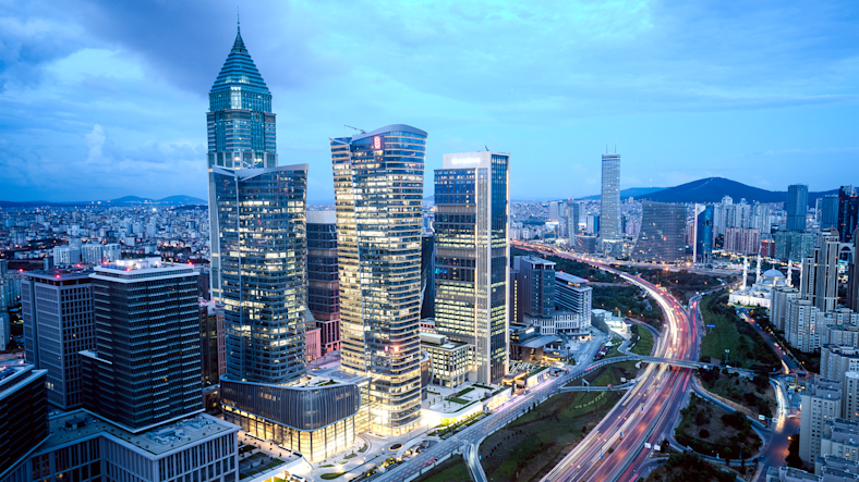 Illuminated skyscrapers rise above the cityscape at twilight, showcasing modern architecture and bustling activity.