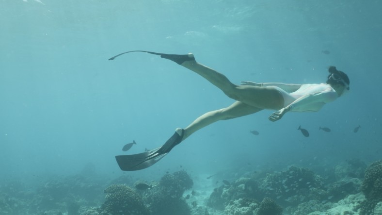 Underwater shot of woman swimming over coral reef wearing Decathlon React diving fins