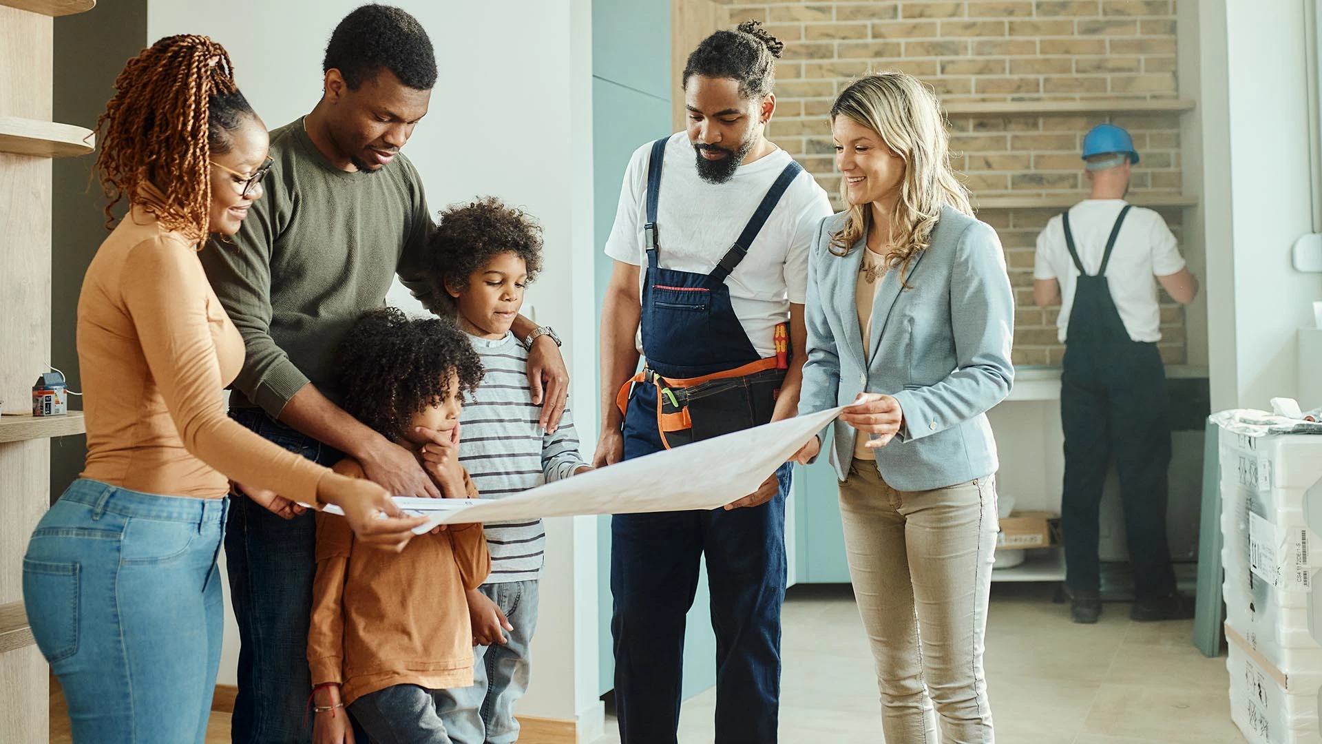 Racially diverse people stand in a building under construction looking at blueprints.