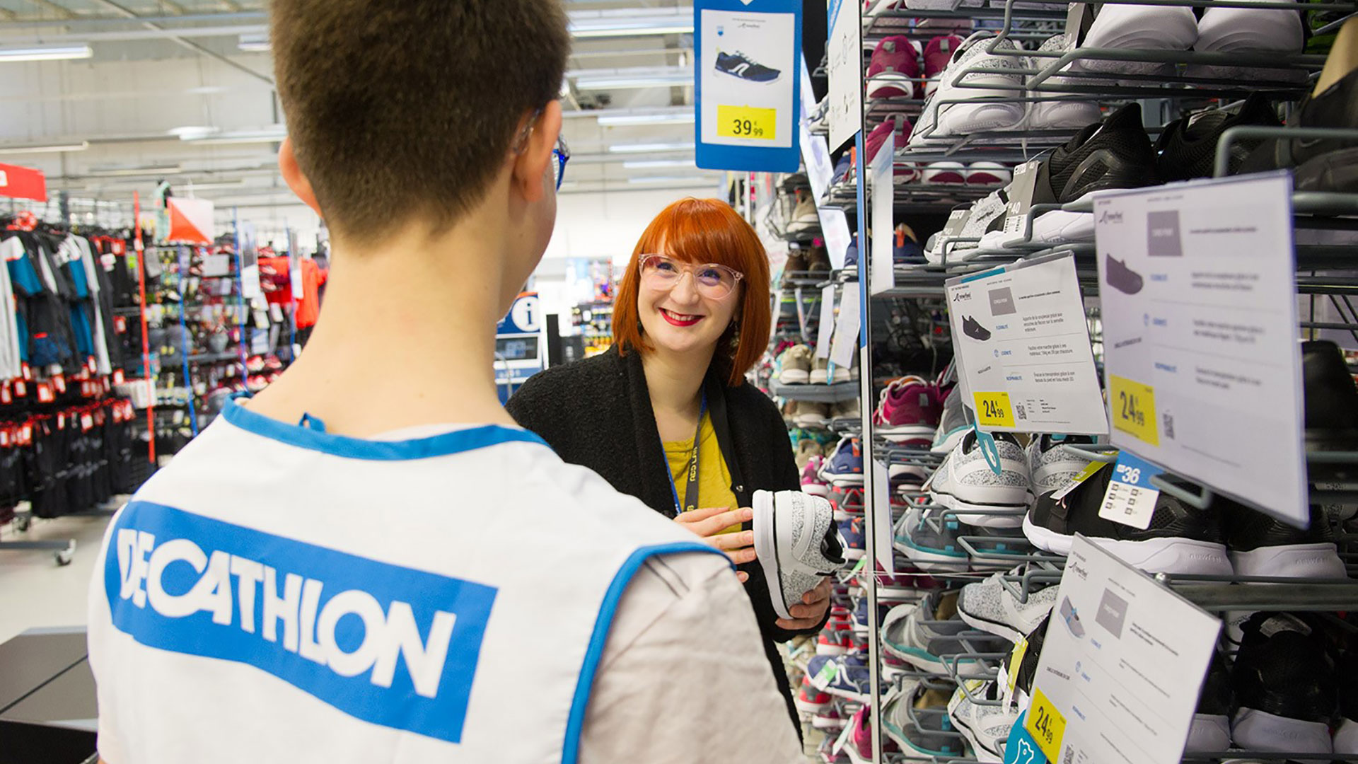 Two Decathlon employees organize a rack with multiple shoe selections.