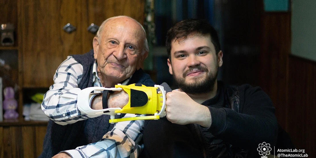 An older man with a prosthetic hand bumps fist with a younger man from Atomic Lab.
