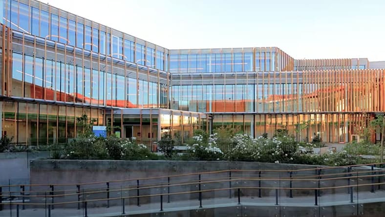 An image shows the outside of the Matta Sur Community Center, a large building with many window panes and an outside garden in Santiago, Chile.