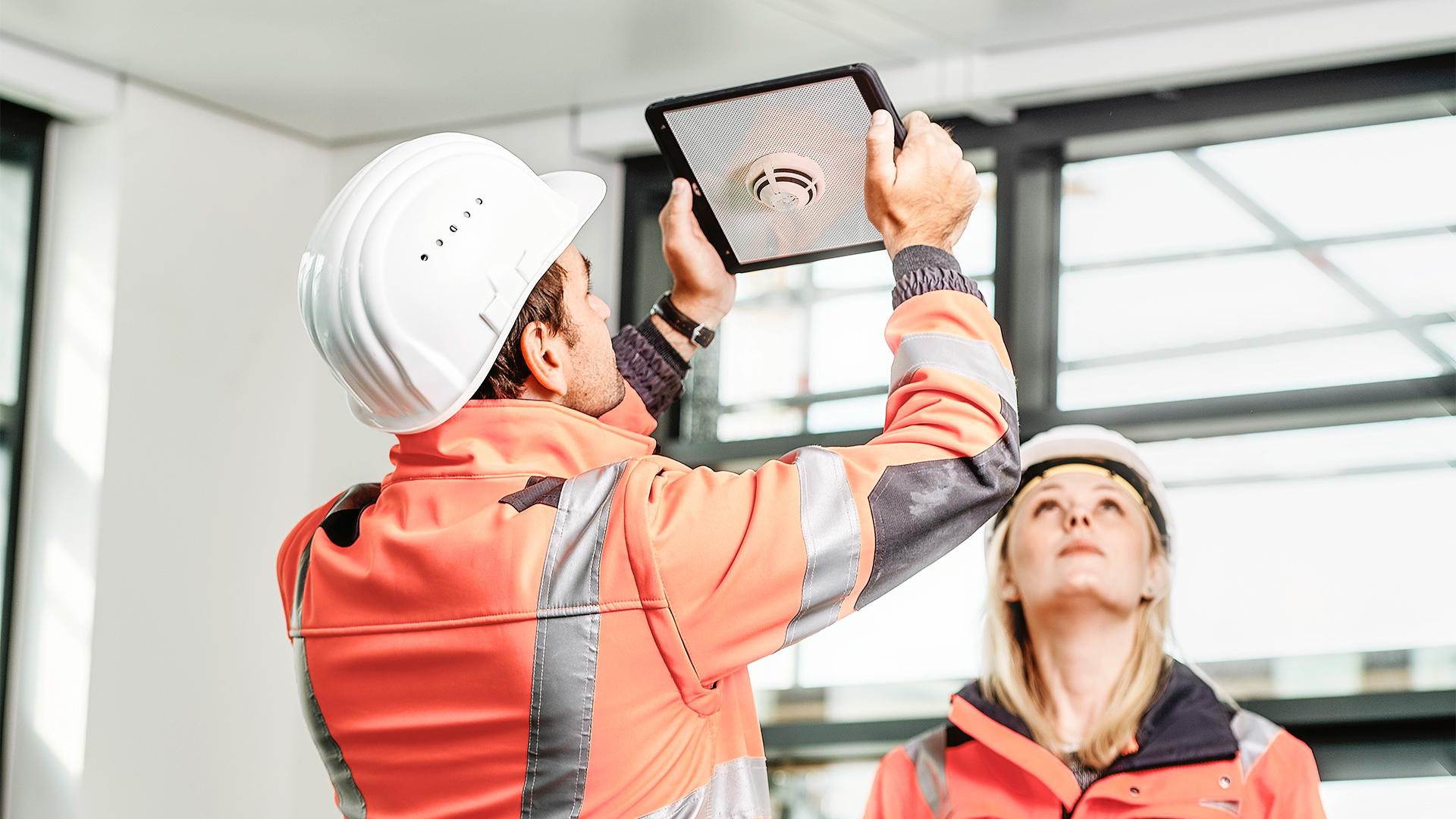 Two people are looking at a smoke detector