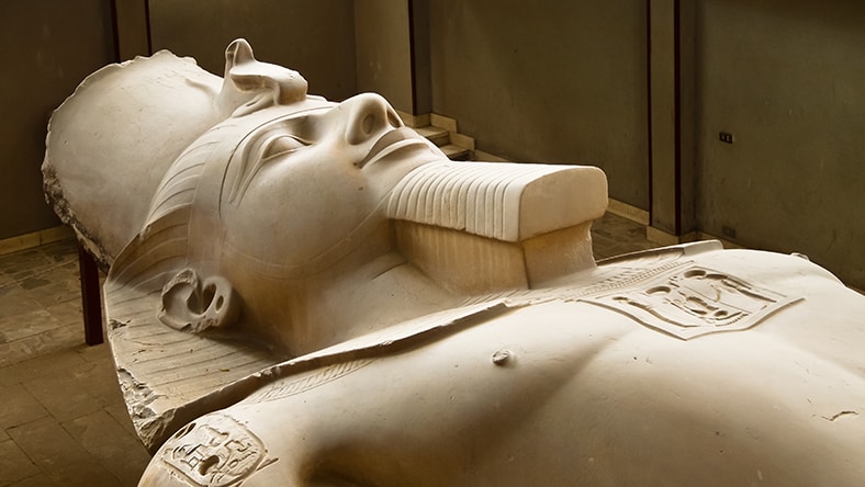 A close-up shows a reclining ancient Egyptian statue indoors.