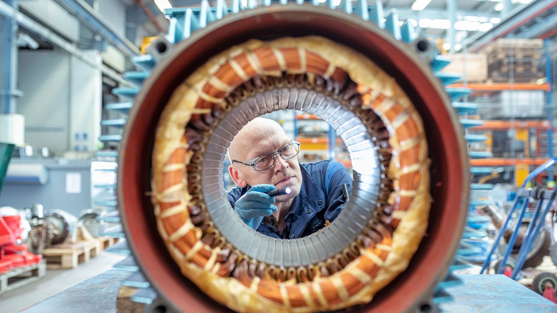 Un ingeniero eléctrico de cierta edad inspecciona el bobinado del estator de un generador en una planta de ingeniería eléctrica.