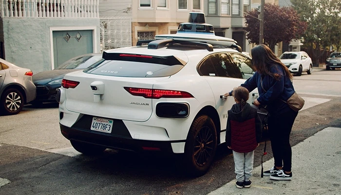 Woman and small boy stand beside white Waymo vehicle 