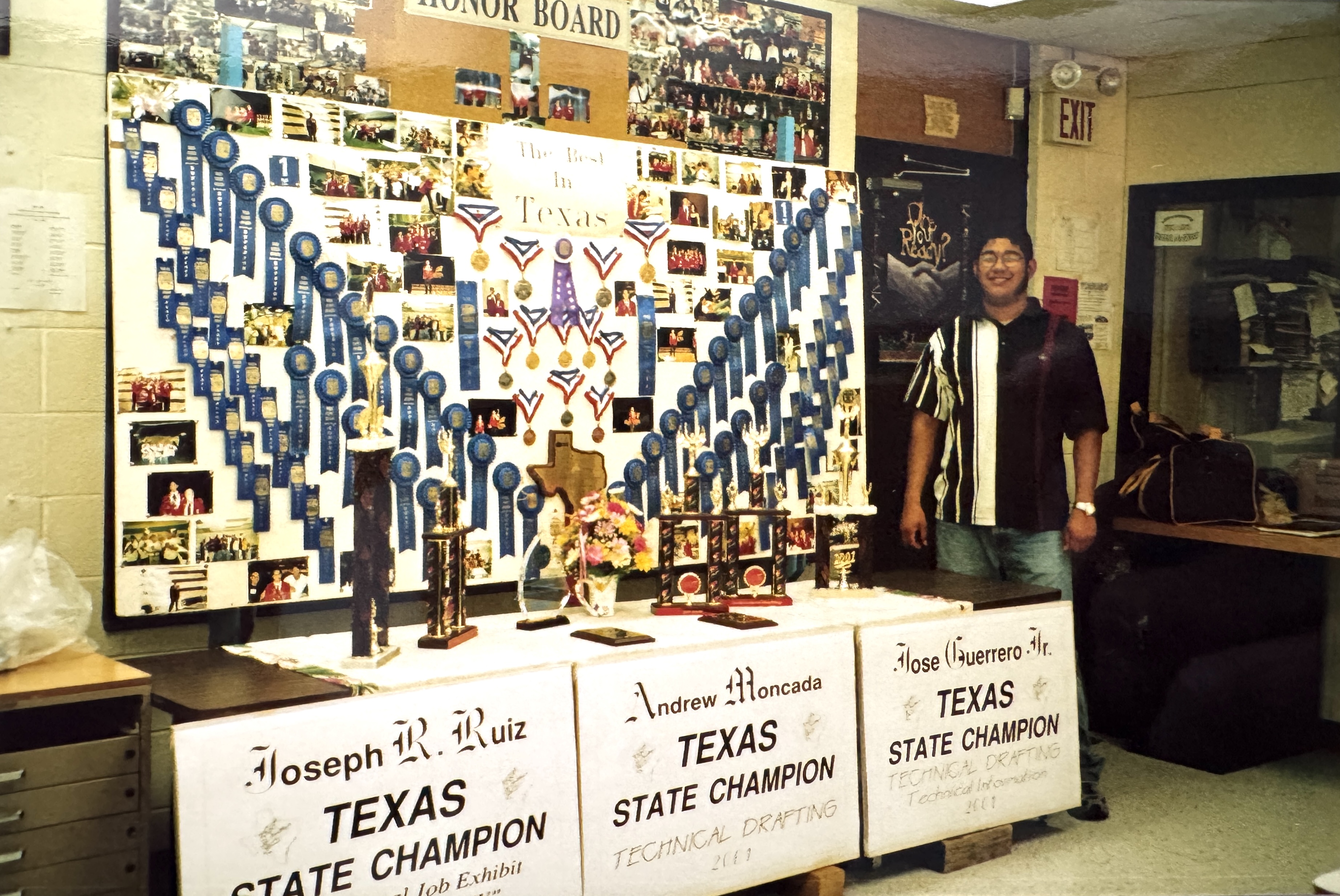 Drew Moncada with table of trophies and awards