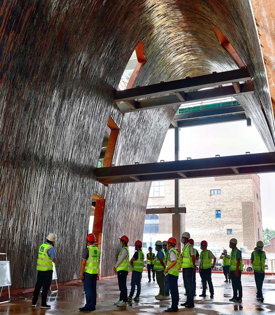 Workers in safety gear stand inside a large arched brick structure under construction.