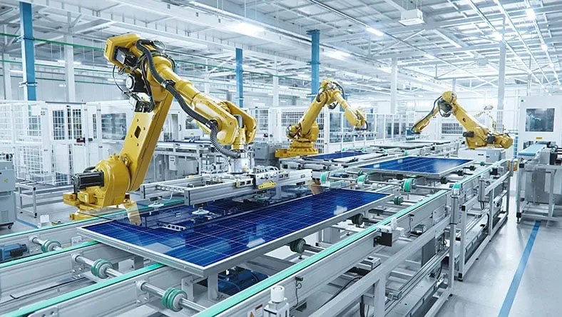 Robots assemble solar panels on a conveyor belt in a factory.