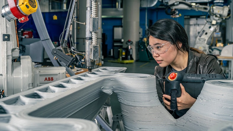 Autodesk Research employees at the Autodesk Technology Center in Boston, use teach pendant on industrial robot arm in additive manufacturing.