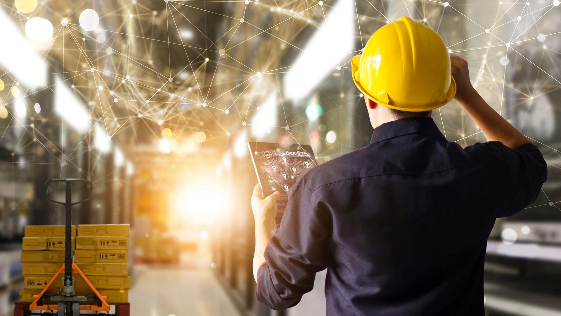A man in a hard hat consults a tablet in a factory scene overlaid with graphics representing connectivity points.  